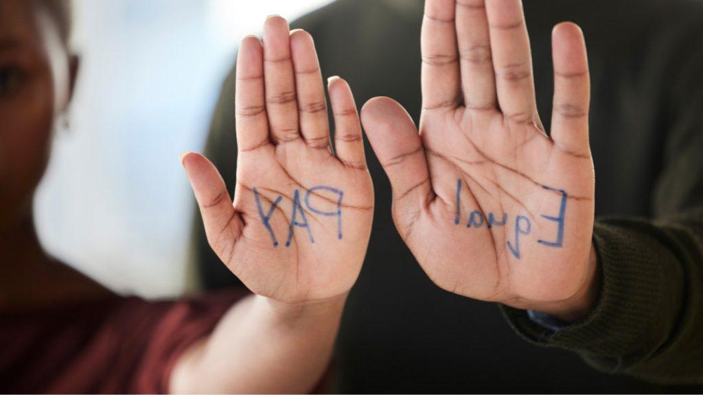 一个男人和一个女人各举起一只手，上面写着同工同酬，以说明歧视和操纵